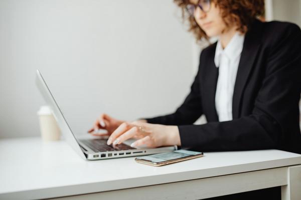 A woman in a black blazer working on a laptop.